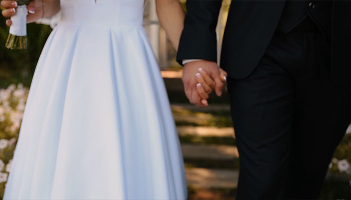 فوتیج عروس و داماد که دست در دست در پس زمینه غروب آفتاب قدم میزنند